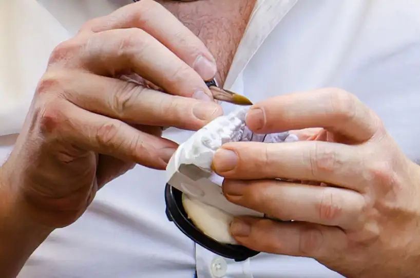 Detailansicht der Hände von Kes Carpenter bei der präzisen Ausarbeitung von festsitzendem Zahnersatz.