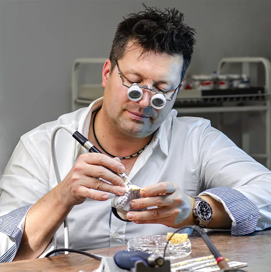 Zahntechniker Kes Carpenter bei der filigranen Ausarbeitung einer Gesamtrehabilitation mit Lupenbrille und Handstück.